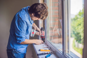 Man in a blue shirt does a window replacement.