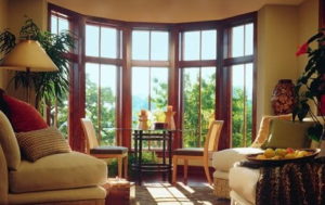 A living room filled with furniture and expansive bow windows with a view of trees